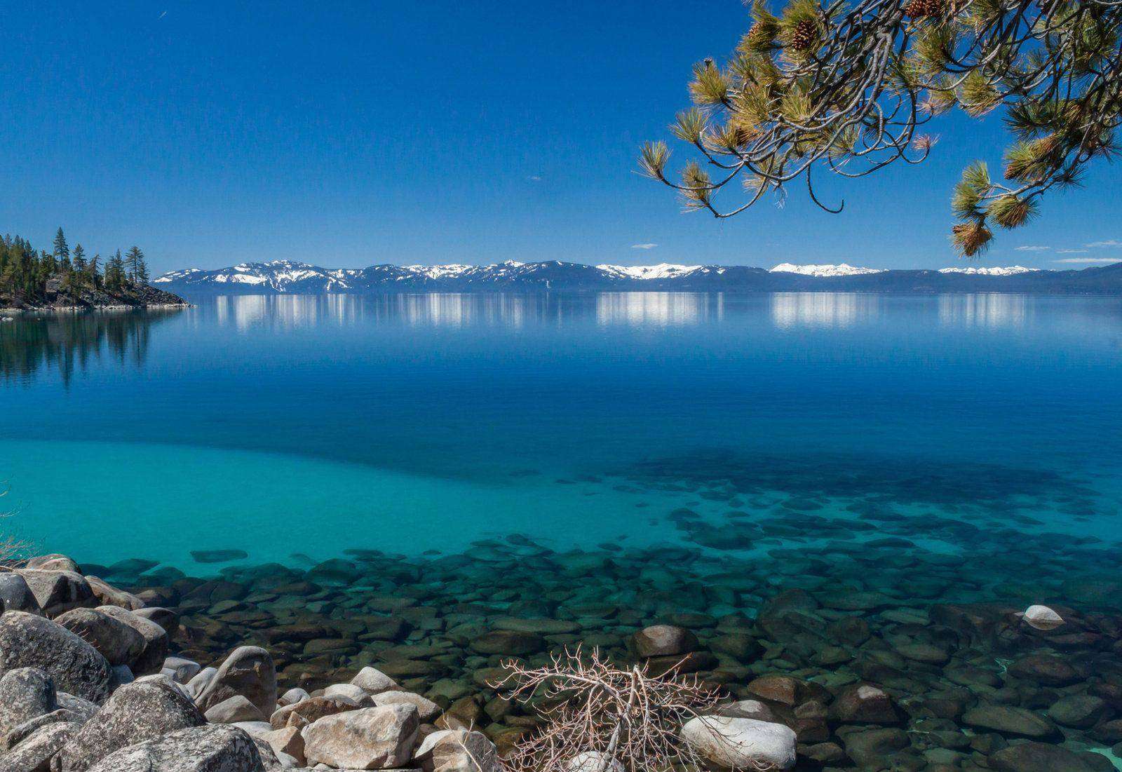 Clear blue water and rocky shoreline of Lake Tahoe with the Sierra behind