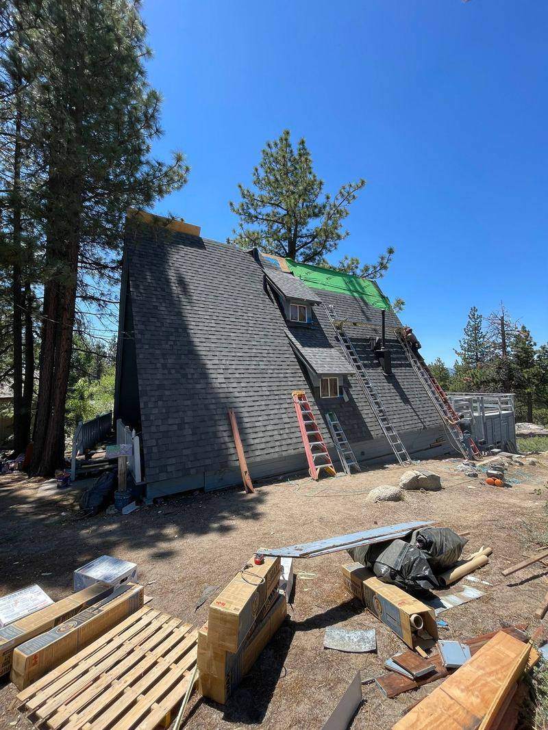Steep A-frame roof replacement in progress with new shingles going on and materials staged below