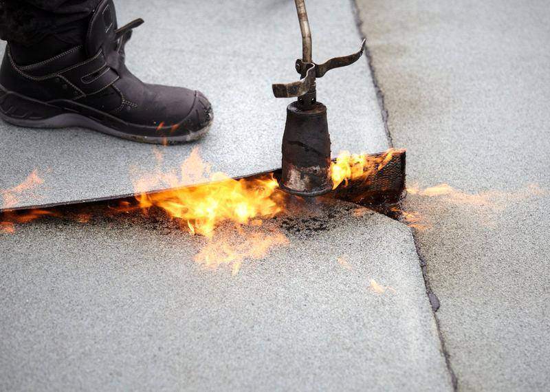 Roofer applying torch-down modified bitumen membrane with a propane torch